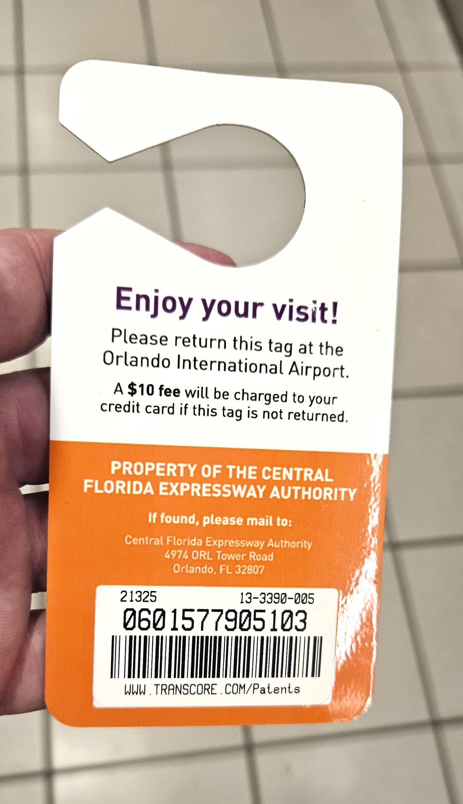Tourist holding Florida Visitor Toll Pass hang-tag device at Orlando International Airport MCO rental car terminal with electronic toll kiosk visible in background